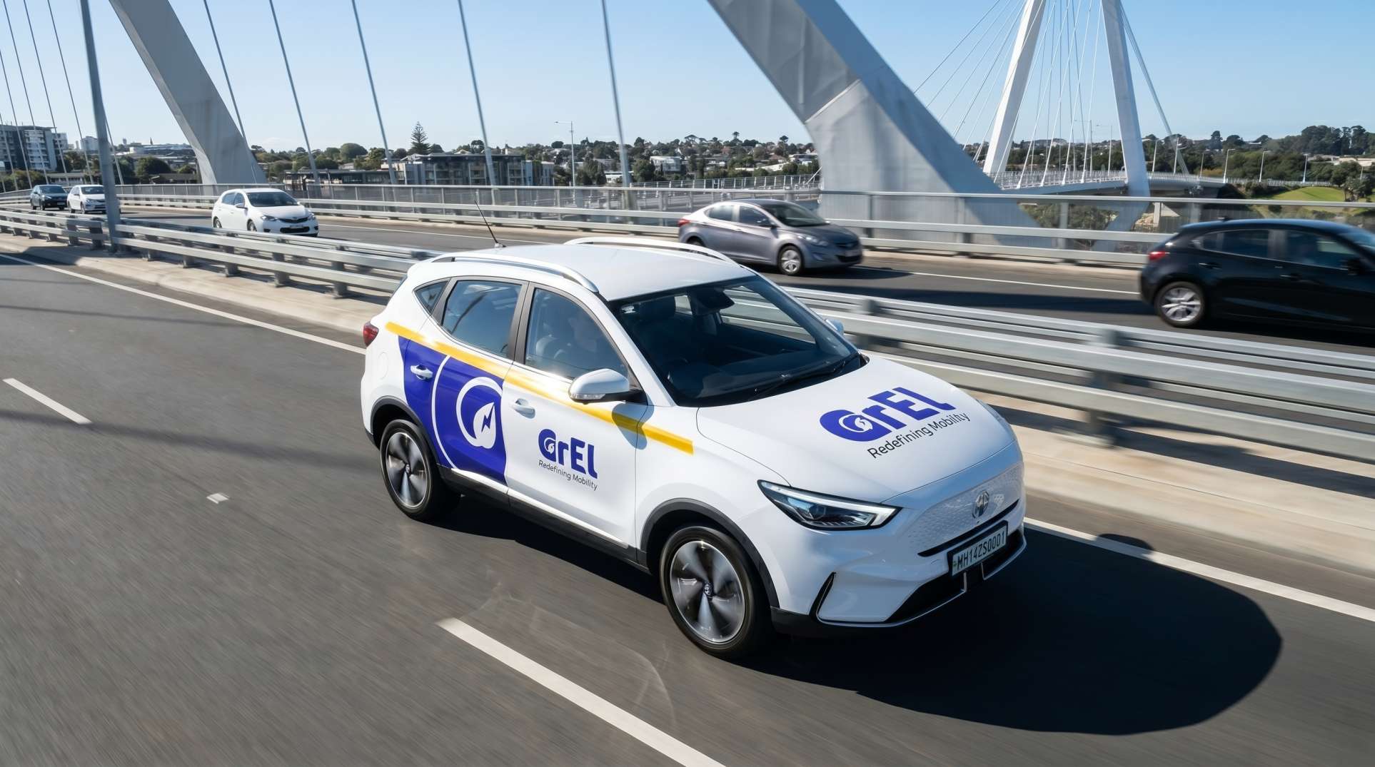 A white GrEL MG ZS EV in violet and amber livery driving across a bridge